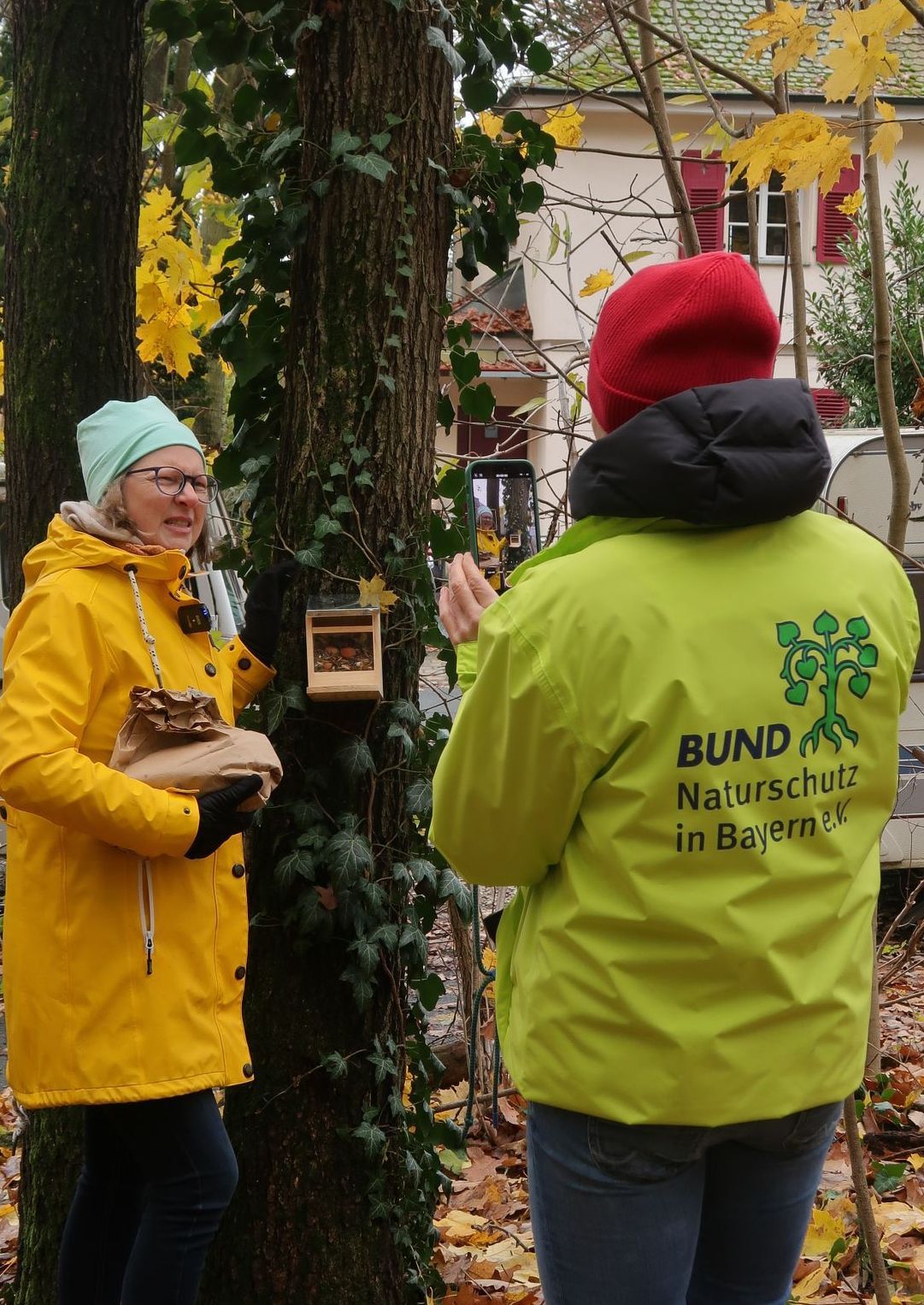 Zwei Personen an einem Futterhäuschen, das in Augenhöhe am Baum hängt.