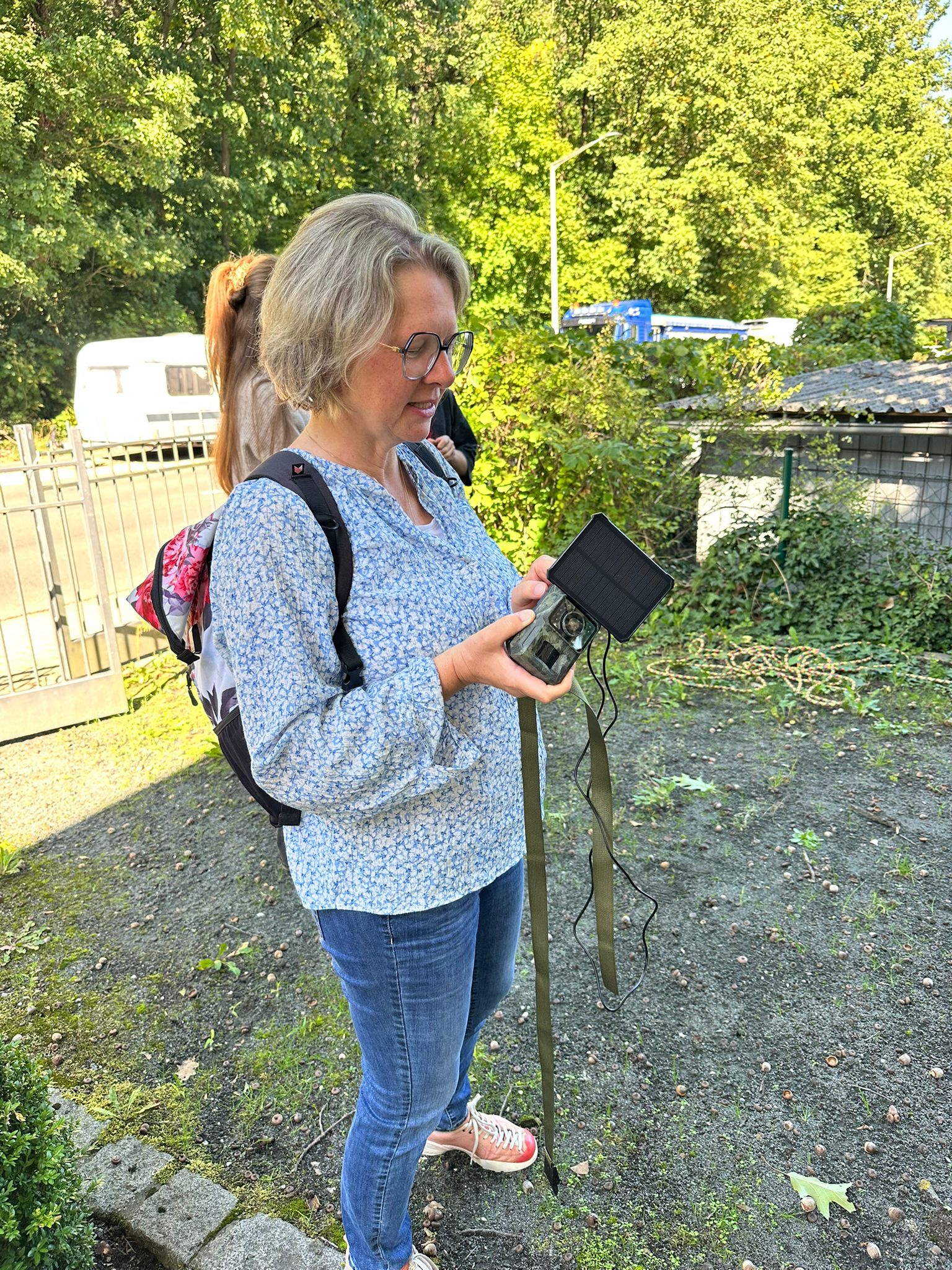 Eine Frau steht im Hof und betrachtet eine Wildtierkamera